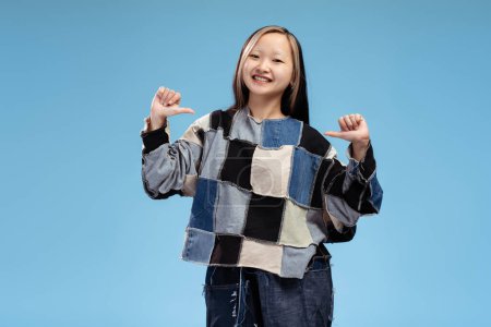 Foto de Retrato de una linda chica asiática sonriente mirando la cámara mostrando los pulgares hacia arriba, posando, aislada en azul. Publicidad, compras, concepto de ventas - Imagen libre de derechos