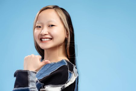 Téléchargez les photos : Portrait de fille asiatique souriante regardant la caméra en studio, montrant les pouces vers le haut, isolé sur fond bleu. Espace de copie. Publicité, achats, concept de vente - en image libre de droit