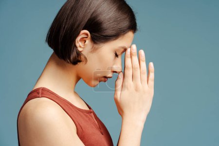 Foto de Mujer pensativa rezando con los ojos cerrados y pensando en problemas aislados sobre fondo azul. Estrés, concepto de depresión - Imagen libre de derechos