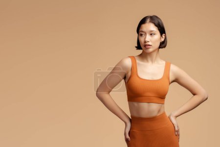Photo for Serious sportswoman wearing fitness uniform, looking away isolated on beige background with copy space. Asian female with stylish hairstyle posing for picture - Royalty Free Image