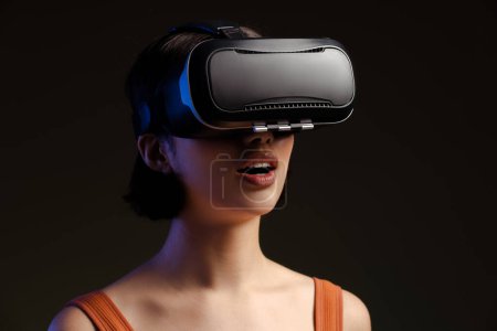Foto de Hermosa mujer jugando a videojuegos con gafas VR aisladas sobre fondo negro. Atractiva joven hembra con tecnología 3D digital - Imagen libre de derechos