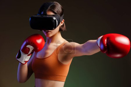 Téléchargez les photos : Portrait de belle femme sérieuse portant des lunettes de réalité virtuelle, en gants de boxe, faisant punch isolé sur fond noir - en image libre de droit