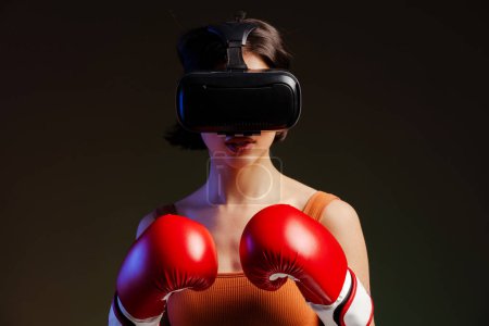 Photo for Studio portrait of young confident athlete woman, professional boxer fighter wearing vr glasses posing in boxing gloves, practicing boxing exercises, over black background - Royalty Free Image