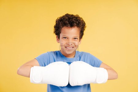 Photo for Cute handsome African American boy boxer wearing white boxing gloves looking at camera standing isolated on yellow background. Concept of competition, sport - Royalty Free Image