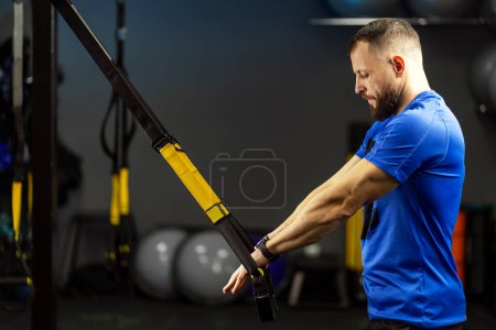 Photo for Attractive, handsome man, strong trainer, athlete doing functional training, holding TRX equipment, standing in modern gym. Concept of sport, healthy lifestyle - Royalty Free Image
