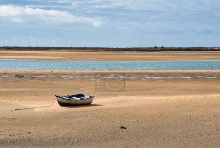 Rustikales altes Boot, das bei Ebbe am Sandstrand vor Anker liegt. Ein verwittertes altes Boot, dessen altes Äußere mit Rost verziert ist, sitzt anmutig im weichen Sand eines ruhigen Strandes bei Ebbe.