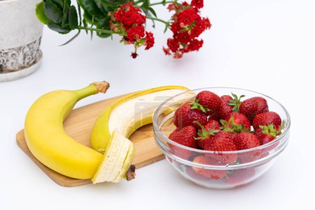 Téléchargez les photos : Fruits bananes et fraises dans un bol en verre avec fleur rouge sur le fond, concept de consommation de fruits frais - en image libre de droit