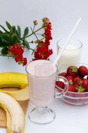 Téléchargez les photos : Boisson au lait, bananes et fraises, dans un verre, sur la table, à côté des fleurs - en image libre de droit