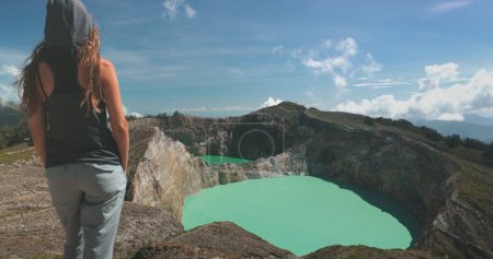 Foto de Mujer turista disfrutar de la vista de la mañana en los lagos volcánicos del cráter azul Kelimutu. Fondo de la naturaleza. Destino de viaje. Hermoso paisaje salvaje. Vacaciones de verano exóticas, senderismo, relajarse. Vista trasera de cerca - Imagen libre de derechos