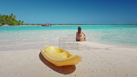 Woman tanning sitting on empty tropical wild beach. Female relax after kayaking enjoy outdoor lifestyle travel on summer holiday vacation. Maldives island luxury resort. Untouched nature sea landscape