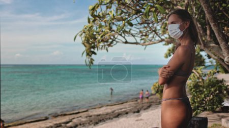 Frau am Strand zieht Sanitätsmaske aus und genießt normales Leben. Sommerurlaub auf der tropischen Insel. Quarantäne und Selbstisolation, epidemische Pandemie, Ende des Covid Coronavirus, Quarantäne über Konzept.