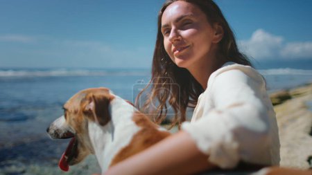 Una mujer está sentada en una roca al aire libre, acompañada de dos perros. La mujer aparece relajada mientras interactúa con los perros, que parecen atentos y juguetones.