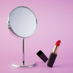 Red lipstick in front of a table mirror on a pastel background. 3D render.