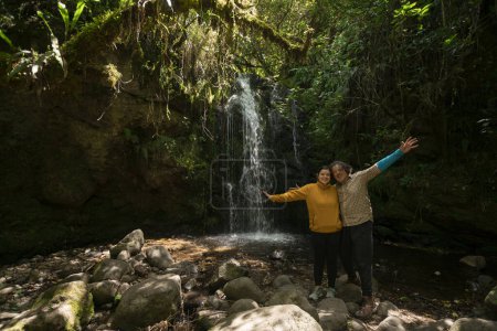 Téléchargez les photos : Portrait d'un jeune couple prenant des photos à côté d'une cascade au milieu d'une forêt lors d'une journée ensoleillée - en image libre de droit