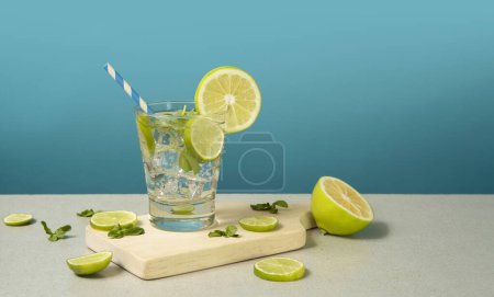 Téléchargez les photos : Cocktail en verre rempli de tranches de glace et de citron garnies de tranches de citron et de sorbet sur une planche de bois sur fond turquoise - en image libre de droit