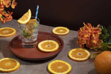 Téléchargez les photos : Cocktail en verre rempli de feuilles de glace et de menthe garnies de tranches d'orange et de sorbet sur une assiette en bois sur une table en céramique avec des tranches d'orange sur fond rouge foncé - en image libre de droit