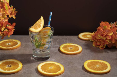 Téléchargez les photos : Cocktail en verre rempli de feuilles de glace et de menthe garnies de tranches d'orange et de sorbet sur une table en céramique avec des tranches d'orange sur fond rouge foncé - en image libre de droit