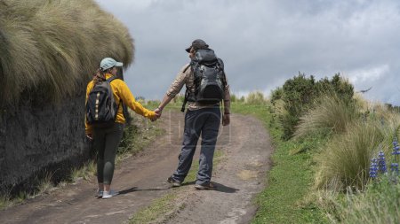 Téléchargez les photos : Jeune couple latino-américain avec des sacs à dos marchant main dans la main sur un sentier au milieu de la friche sur une montagne par une journée ensoleillée - en image libre de droit