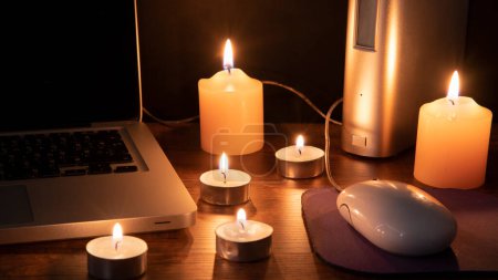 Téléchargez les photos : Concept Blackout, 6 bougies allumées illuminant l'espace de travail avec un ordinateur portable sur fond noir - en image libre de droit
