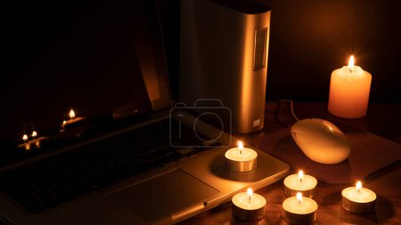 Téléchargez les photos : Concept Blackout, 6 bougies allumées illuminant l'espace de travail avec un ordinateur portable sur fond noir - en image libre de droit