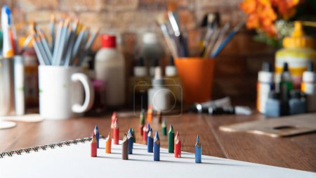 Téléchargez les photos : Petits crayons de couleur sur papier blanc sur une table en bois avec des fournitures d'art en arrière-plan hors foyer - en image libre de droit