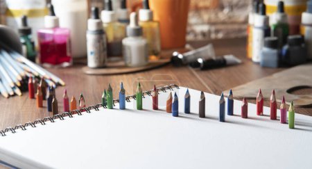 Téléchargez les photos : Petits crayons de couleur sur papier blanc sur une table en bois avec des fournitures d'art en arrière-plan hors foyer - en image libre de droit