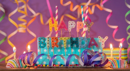 Téléchargez les photos : Lettres de différentes couleurs formant la phrase HAPPY BIRTHDAY, avec des bougies allumées sur fond violet flou avec des banderoles - en image libre de droit