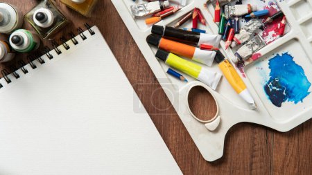 Téléchargez les photos : Vue du dessus de la table en bois avec crayons, tubes de peinture, fournitures d'art, bouteilles d'encre, variété de pinceaux sur papier blanc - en image libre de droit