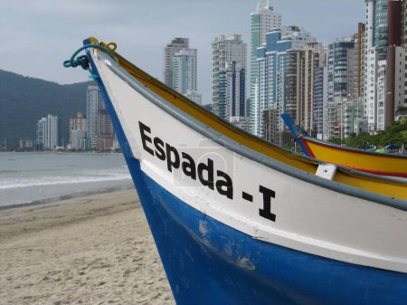 Photo for Fishing boat on the sands of Balneario Camboriu beach in Santa Catarina, sea and buildings in the background. - Royalty Free Image