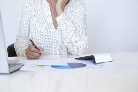 Foto de Mujer de mediana edad en camisa blanca analizando estadísticas y gráficos con su computadora - Imagen libre de derechos