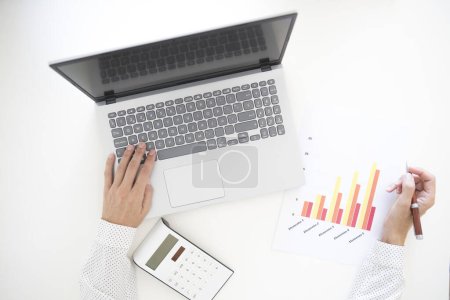 Foto de Manos de una mujer de mediana edad que trabaja con una computadora portátil analizando un gráfico y con una calculadora. - Imagen libre de derechos