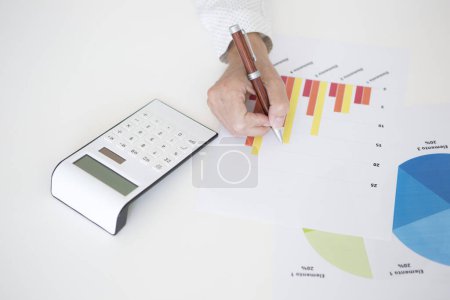 Foto de Detalle de manos de mujer de mediana edad en camisa blanca trabajando con documentos con gráficos financieros y estadísticas - Imagen libre de derechos
