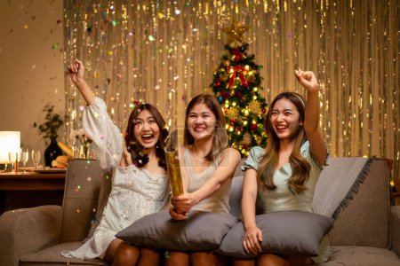 Photo for Young beautiful people is sitting on the couch to playing and shooting firecracker or poppers confetti party with enjoying while celebrating in new year party at home. - Royalty Free Image