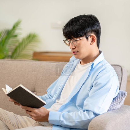 Photo for Businessman in casual is sitting on comfortable sofa to relaxation with hobby of reading the book while leisure with cozy lifestyle in living room at home. - Royalty Free Image
