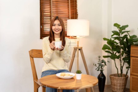 Foto de Mujer joven lesbiana mirando cámara a sonreír y disfrutar con el consumo de chocolate caliente, mientras que pasar tiempo para relajarse en la sala de estar en casa. - Imagen libre de derechos