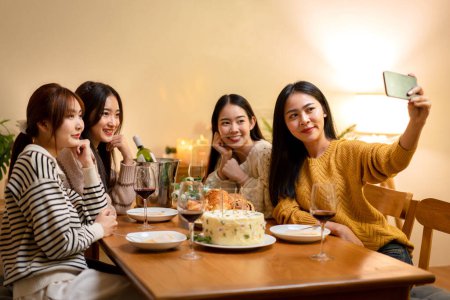 Photo for Young people sitting on the couch to smiling with enjoying and using smartphone to selfie together while dinner and celebrating in new year party at home. - Royalty Free Image
