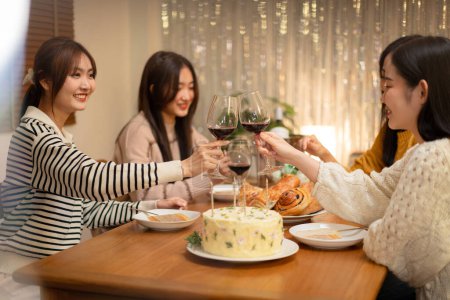 Photo for Young smiling woman drinking and clinking glass of wine to toasting with happiness while celebrating in new year party at home. - Royalty Free Image