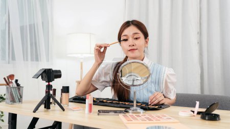 Photo for Young beauty influencer is using mascara product to testing and recommend cosmetic while recording video on camera for share on social media or web blogger in studio. - Royalty Free Image