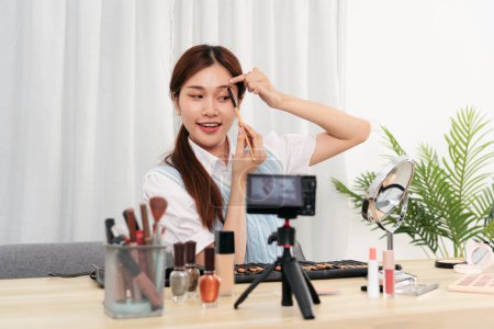 Photo for Young beauty influencer using brush with eyebrow to testing and recommend cosmetic product while recording video on camera for share on social media or web blogger in studio. - Royalty Free Image