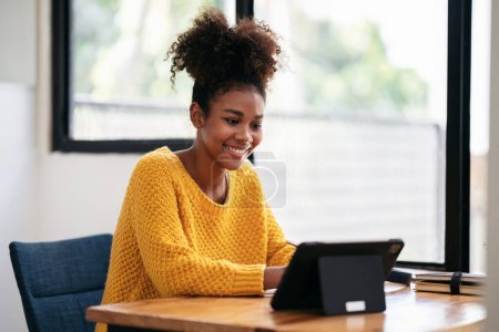 African american student woman in sweater using digital tablet to watching e-learning and studying lesson online class while sitting on the desk to learning knowledge and education in university. Poster 646177514