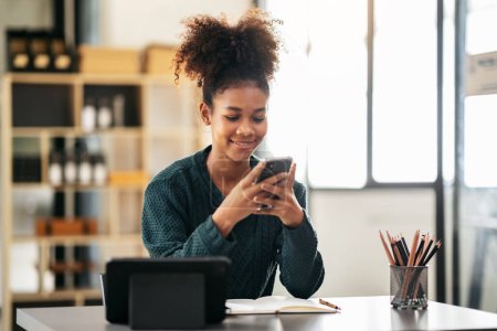 Photo for African american student woman in sweater using smartphone after watching e-learning and studying lesson online class on tablet while sitting to learning knowledge and education in university. - Royalty Free Image