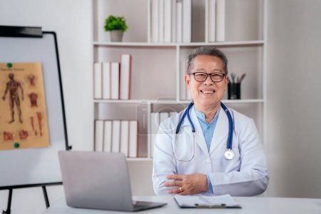 Photo for Confident senior male doctor with stethoscope to working on laptop about healthcare and prescription document of patient in hospital while sitting with arm crossed and smiling to looking at camera. - Royalty Free Image
