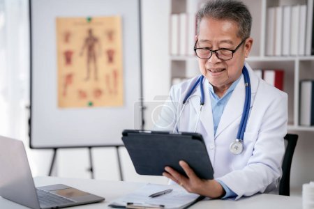 Photo for Senior male doctor with stethoscope is working on laptop and searching treatment of disease information on tablet while diagnosis of patient disease and writing prescription on clipboard in hospital. - Royalty Free Image