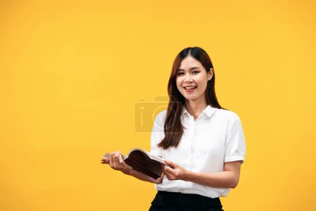 Photo for Young asian woman wearing white short sleeve shirt and holds holy bible to reading and praying to god about spirituality faith worship isolated over yellow background. - Royalty Free Image