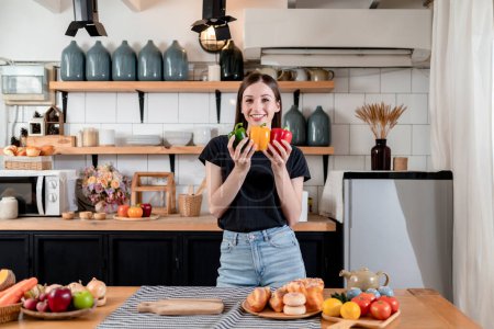Photo for Woman holding colorful bell pepper in her hands with enjoying while preparing fresh vegetable and fruits with organic products on the table to cooking for healthy meal in modern kitchen at home. - Royalty Free Image