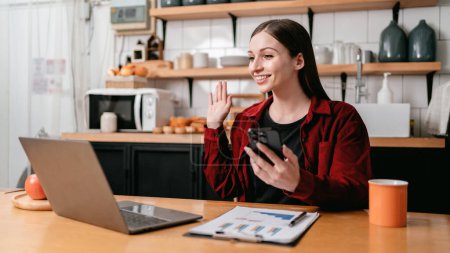 Photo for Young businesswoman using laptop to video conference and greeting with partners for meeting about new business project while sitting to working in kitchen at home. - Royalty Free Image