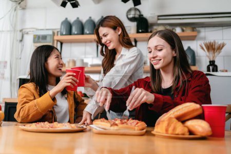 Photo for Group of friends clinking glass of beverage and cutting slice of italian pizza for dinner meal while having enjoying with party to celebration for weekend in the kitchen at home. - Royalty Free Image
