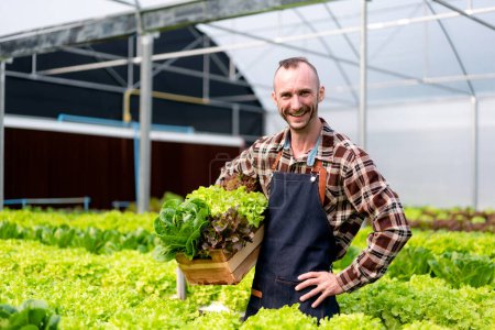 Foto de Joven agricultor agronegocio inteligente sonriendo y sosteniendo verduras hidropónicas orgánicas en la cesta para preparar la exportación para vender. - Imagen libre de derechos