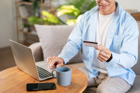 Photo for Businessman in casual is sitting on comfortable sofa and holding credit card to entering number and data to purchase product on laptop for shopping online while leisure with cozy lifestyle at home. - Royalty Free Image