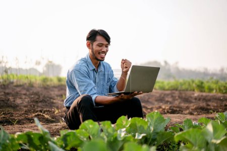 Photo for Smart farmer raising arm to celebrate after using laptop to examining quality crop of cabbage vegetables successful while working and planning system control with technology at agricultural field. - Royalty Free Image